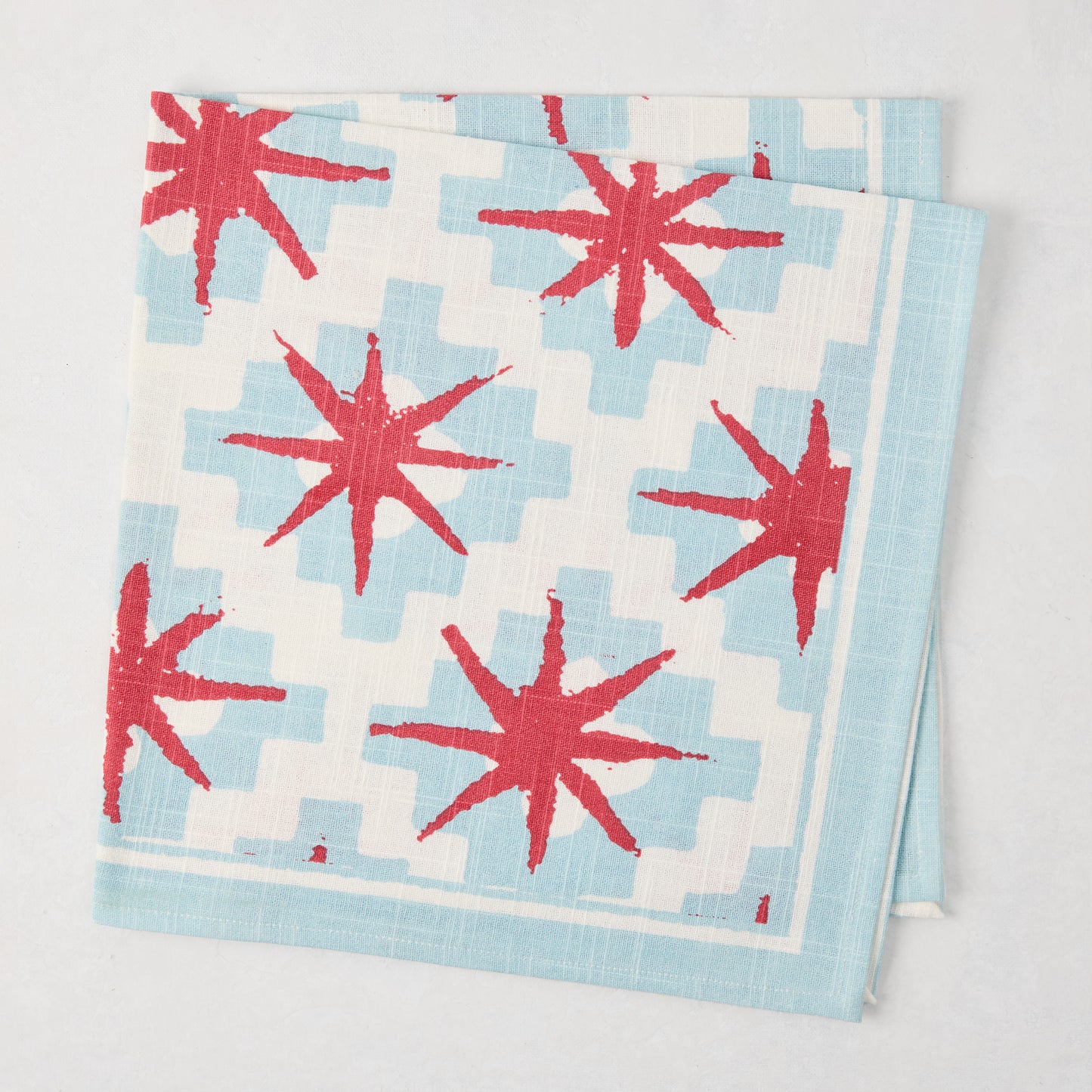 Peter Dunham + Hudson Grace Blue Starburst Printed Napkin, 100% cotton slub, red starbursts on blue geometric.