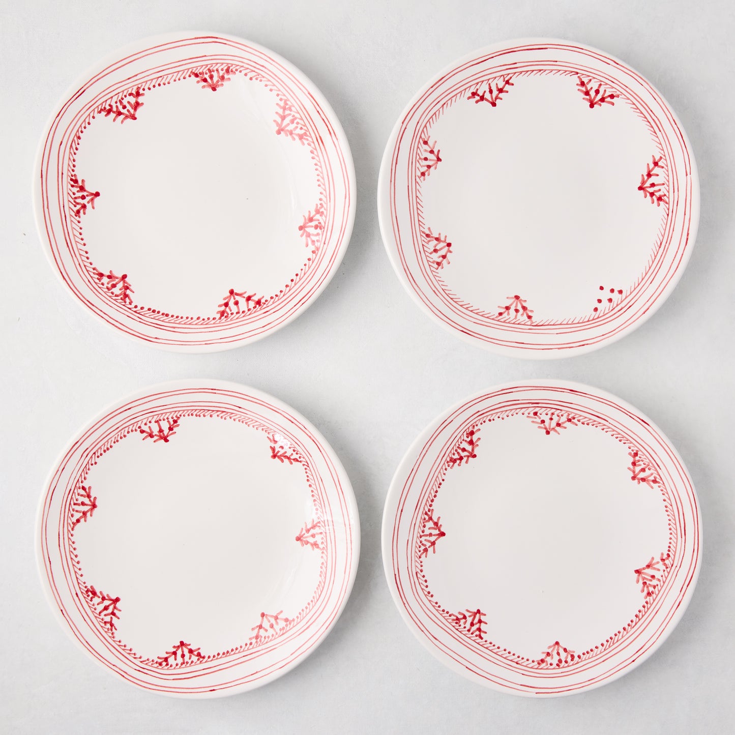 Four white Peter Dunham + Hudson Grace Red Fez salad plates with hand-painted red borders.