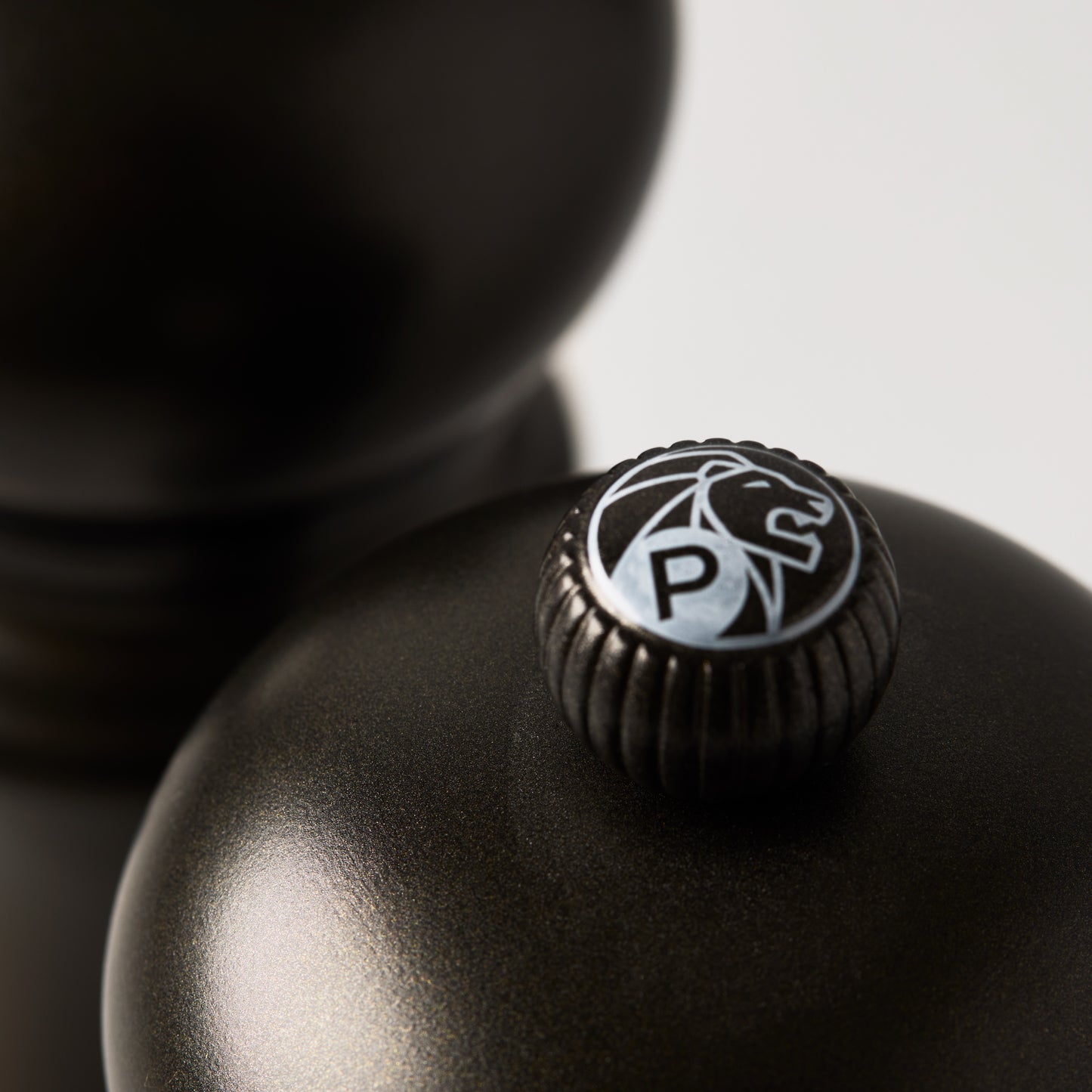 Close-up of a matte black Peugeot Paris pepper mill with a silver "P" and lion logo on top.