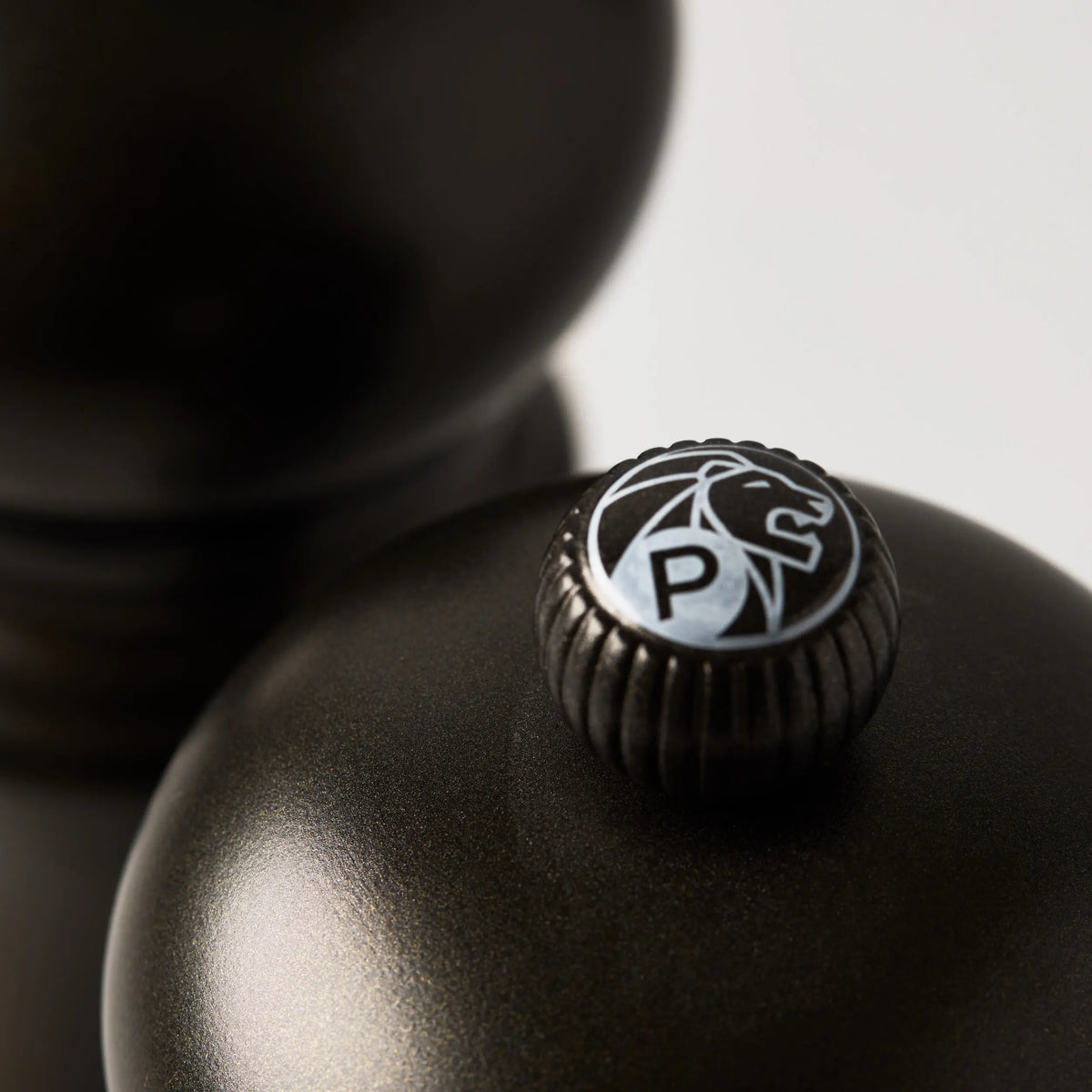 Close-up of a matte black Peugeot Paris pepper mill with a silver "P" and lion logo on top.