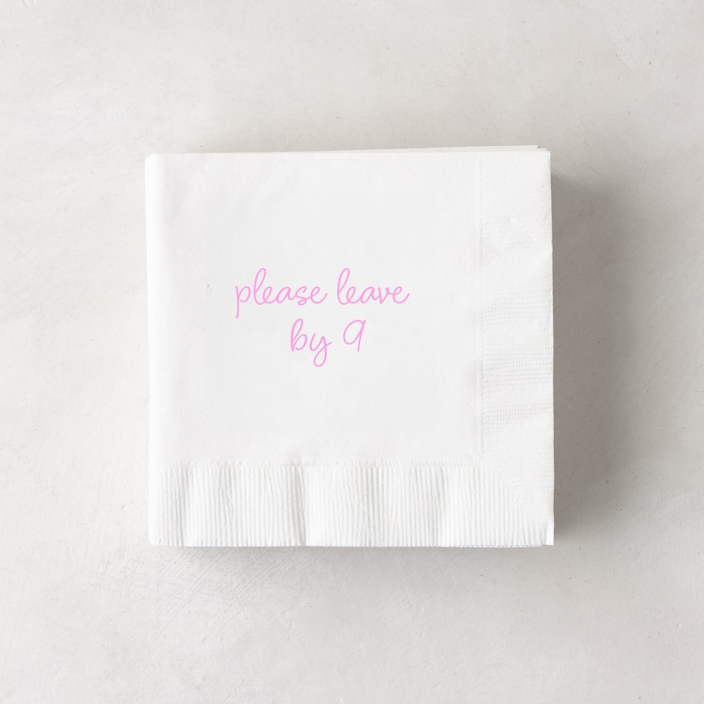 White 3-ply paper cocktail napkin with "please leave by 9" in pink script, 5.5" square.