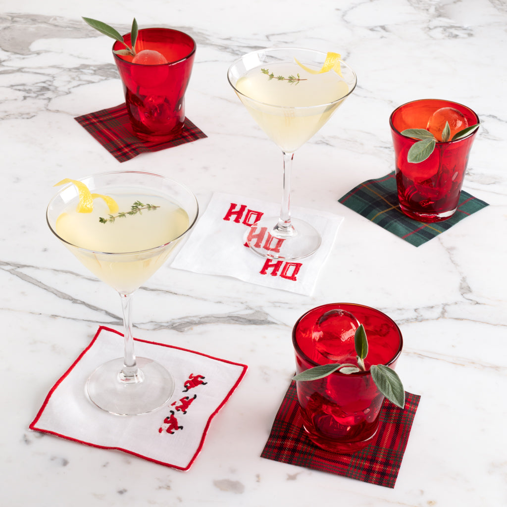 Red tartan tear-off cotton cocktail napkins, some with Santa or "HO HO HO" embroidery, under drinks.