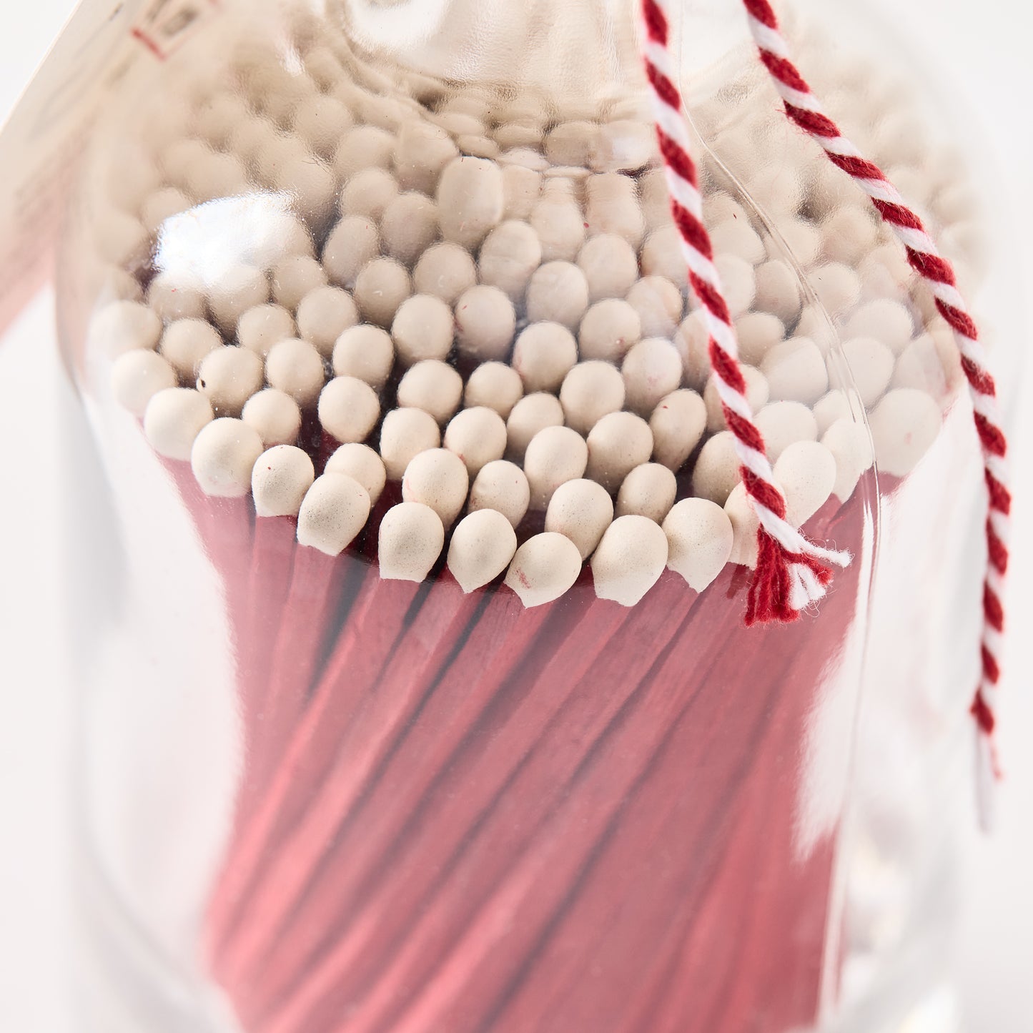 Glass bottle of oversized red matches with white tips, tied with red and white twine.