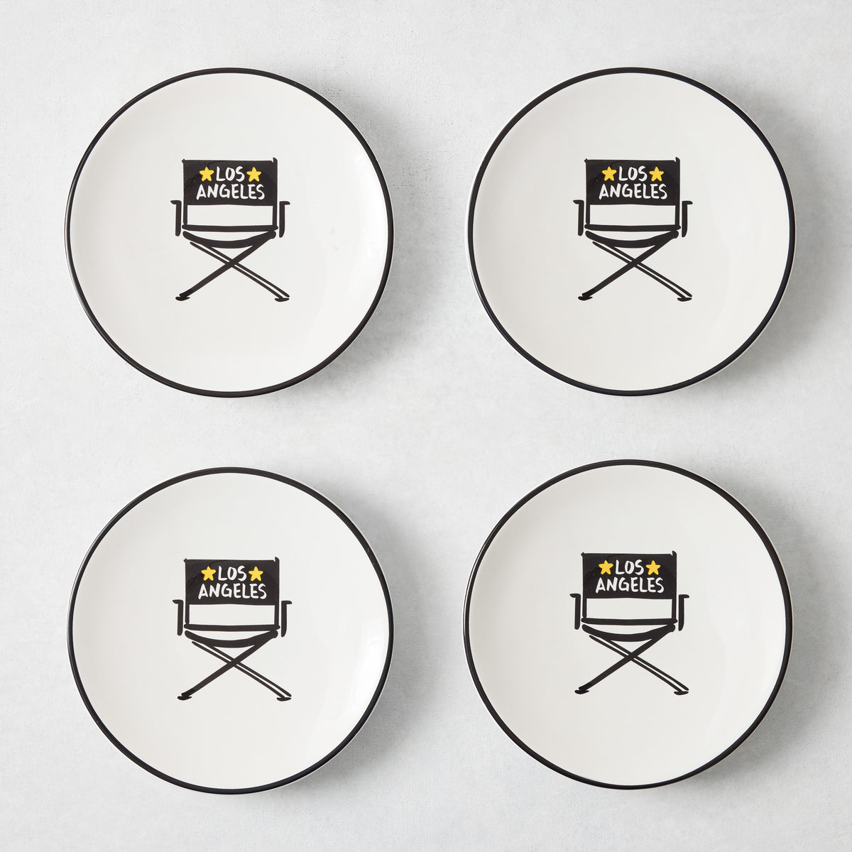 Set of four white appetizer plates with black rims and hand-painted Los Angeles director's chair illustrations.
