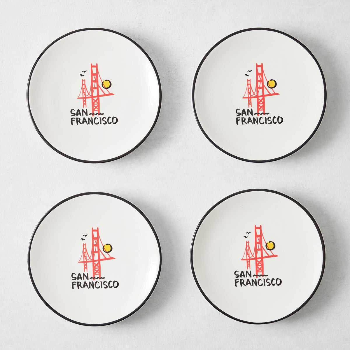 Set of four white appetizer plates with black rims and hand-painted Golden Gate Bridge San Francisco illustrations.