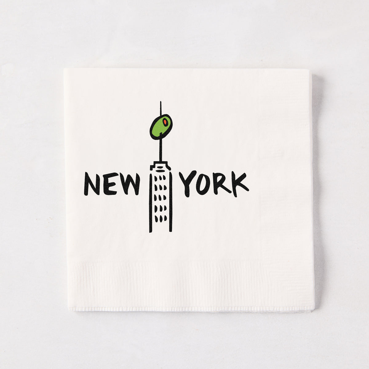 White 5.5-inch 3-ply paper cocktail napkin with a black New York skyscraper illustration topped with a green olive.