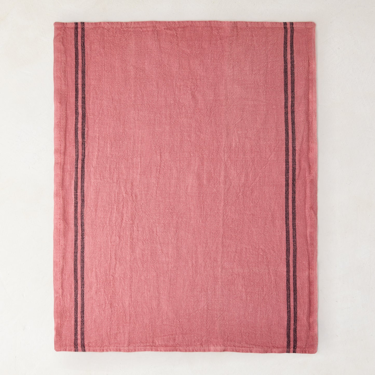 Rosy pink French linen tea towel with dark vertical stripes on each side.