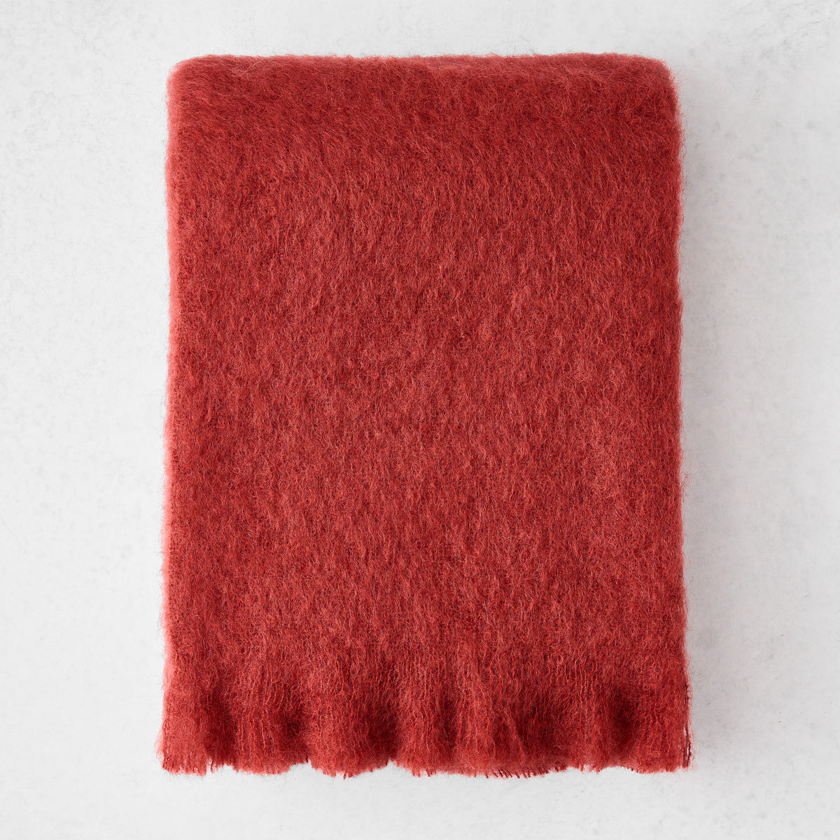 Russet red solid mohair throw blanket with a thick, fuzzy texture and fringed edges on a light background.