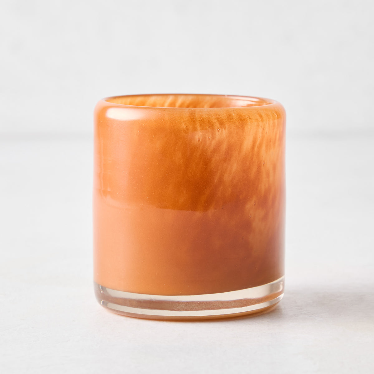 Small mouth-blown rust red glass votive candle holder with a thick base and translucent, marbled finish.