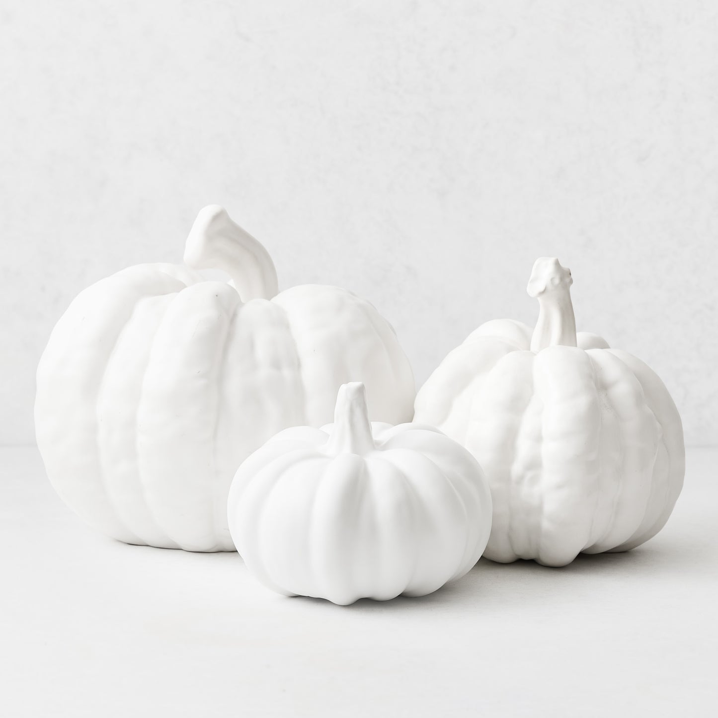 Three small, matte white ceramic pumpkins of varying sizes arranged on a white surface.