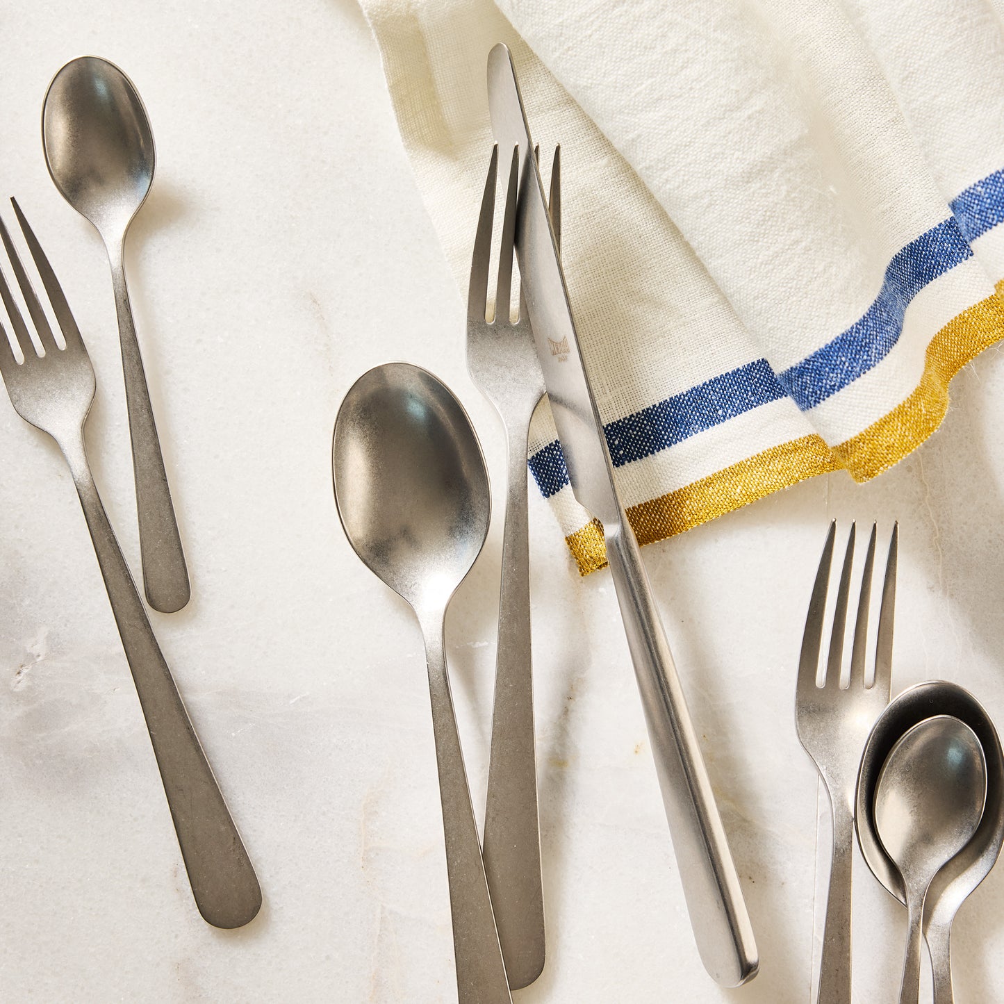 Stoccolma Pewter 5-piece flatware set, 18/10 stainless steel with a mirror finish, on marble.