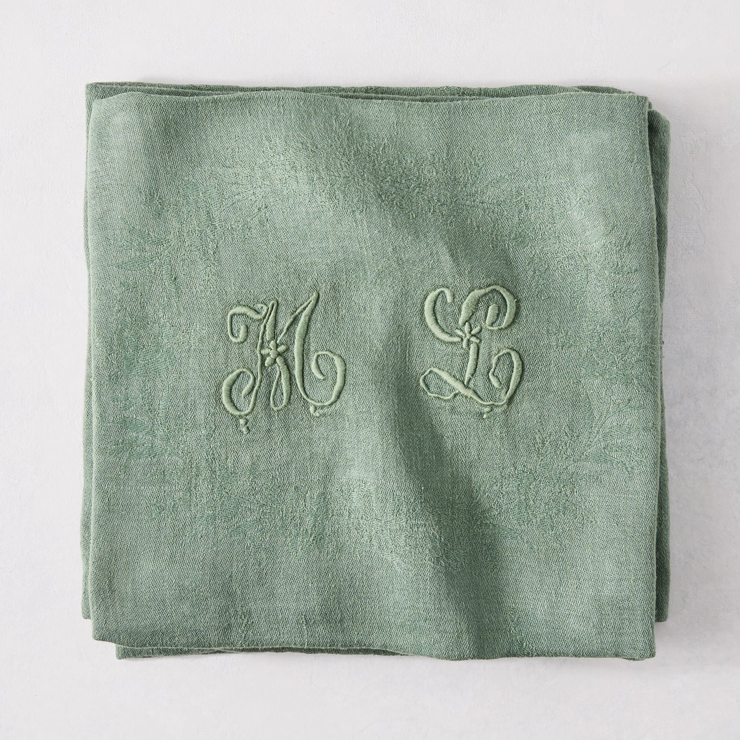 Folded Swiss Chard green antique French monogram napkin, linen-cotton blend, with embroidered "ML" initials.