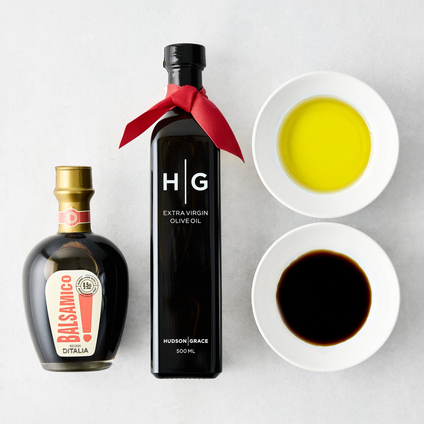 Hudson Grace olive oil, balsamic vinegar, and two white dipping bowls with oil and vinegar.