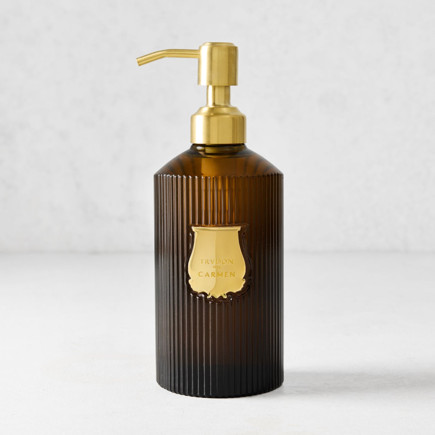 Trudon Carmen liquid hand soap in a ribbed amber glass bottle with a gold pump and label.