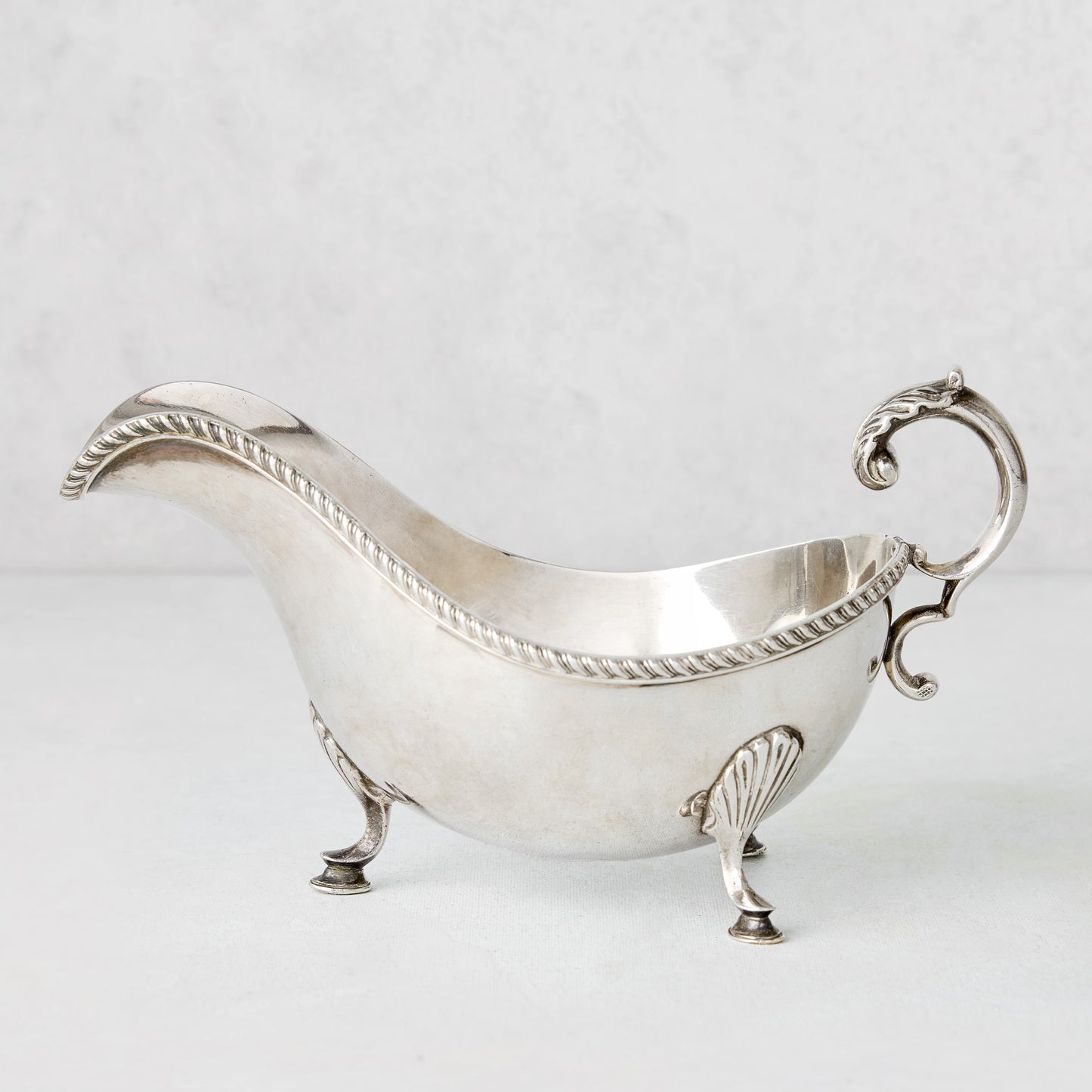 Vintage silverplate gravy boat with ornate handle, rope trim, and shell feet.