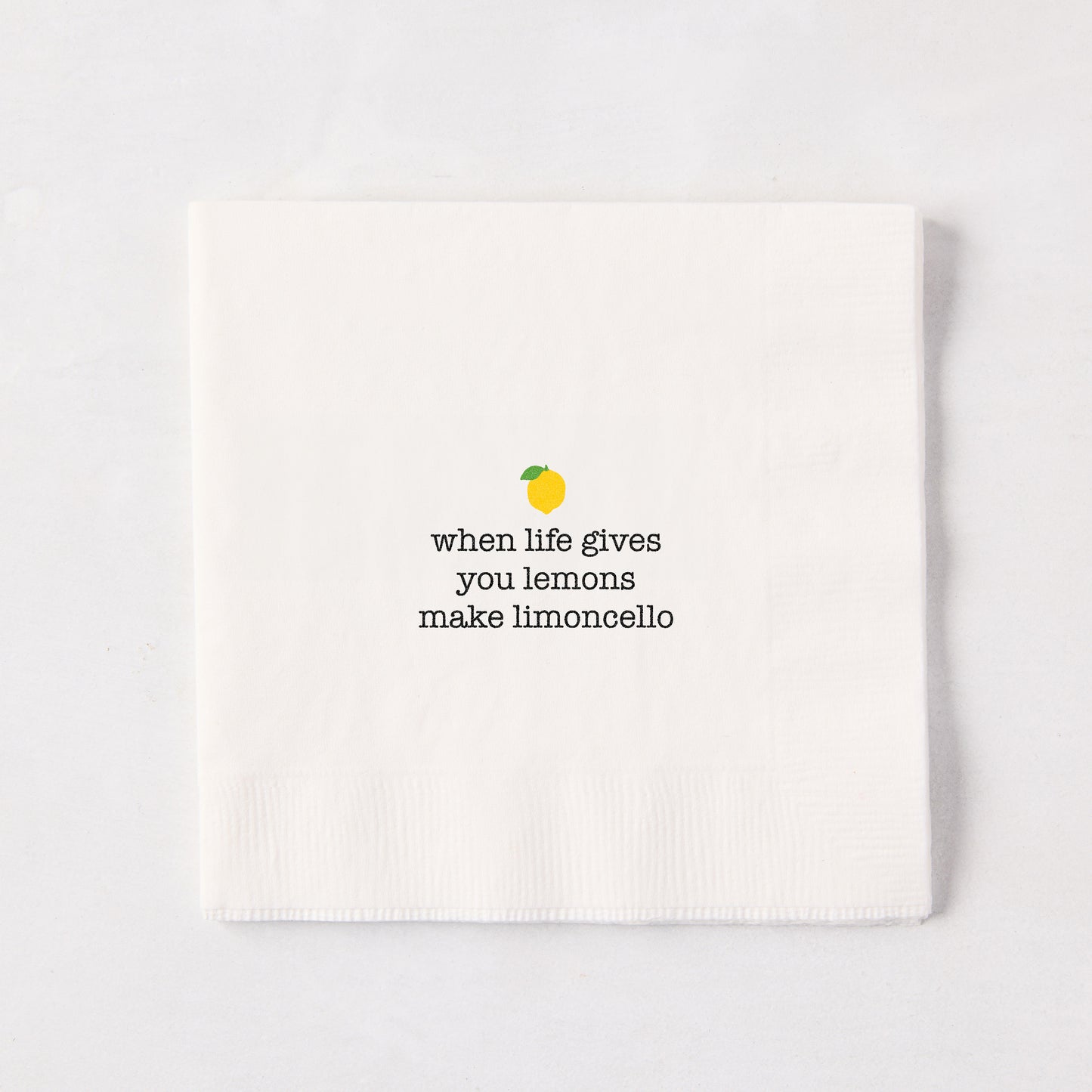 White 5.5" square paper cocktail napkin with "when life gives you lemons make limoncello" text and lemon graphic.