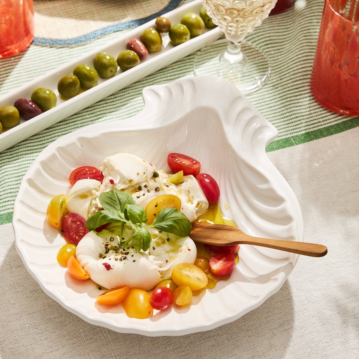 White ceramic shell-shaped serving tray with burrata, cherry tomatoes, and basil.