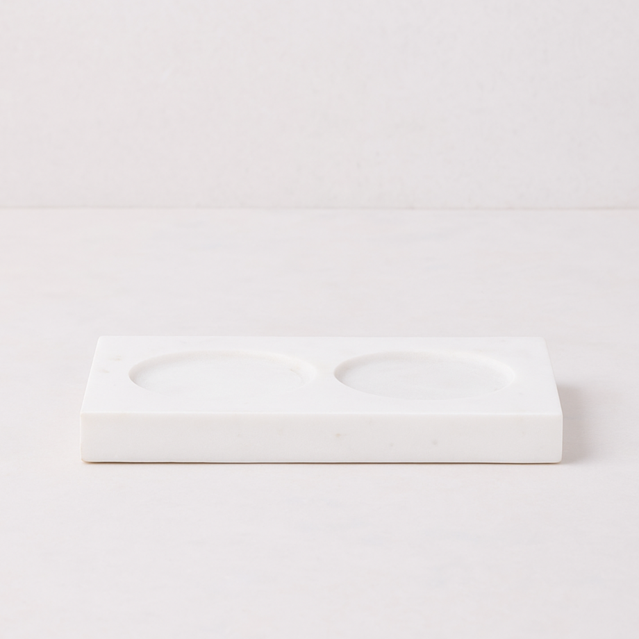 White marble rectangular tray with two circular indentations for soap and lotion bottles.