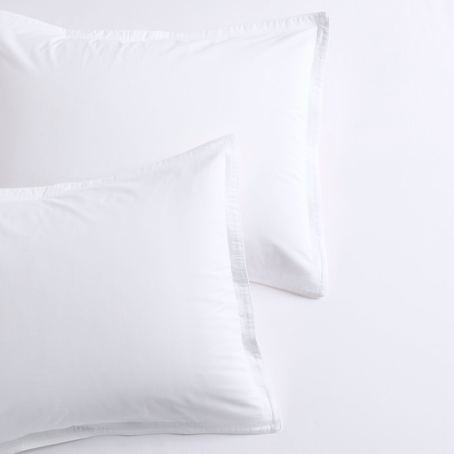 Two white percale pillow shams with delicate white piping and double-stitch detailing.