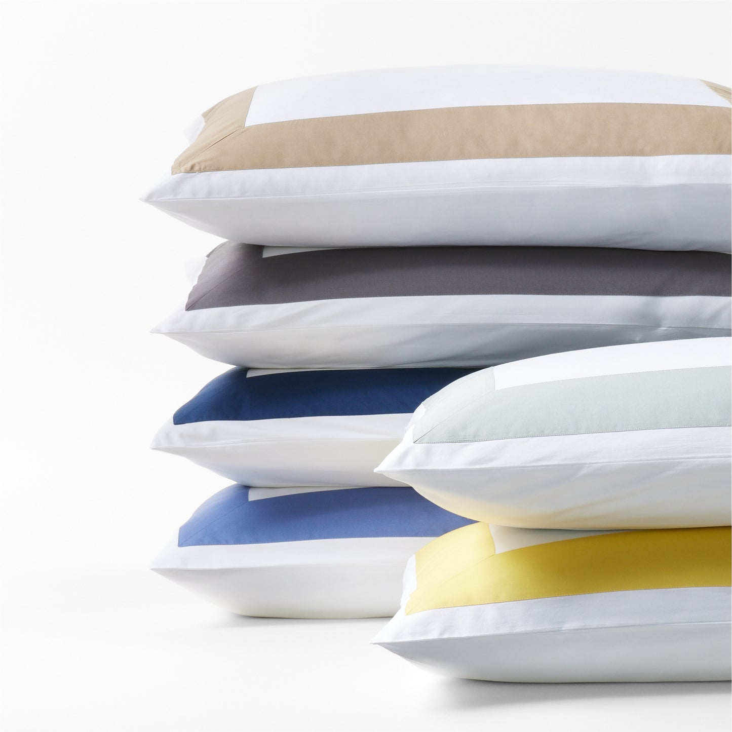 Stacked percale pillow shams in yellow, tan, gray, blue, and light blue with a wide band.