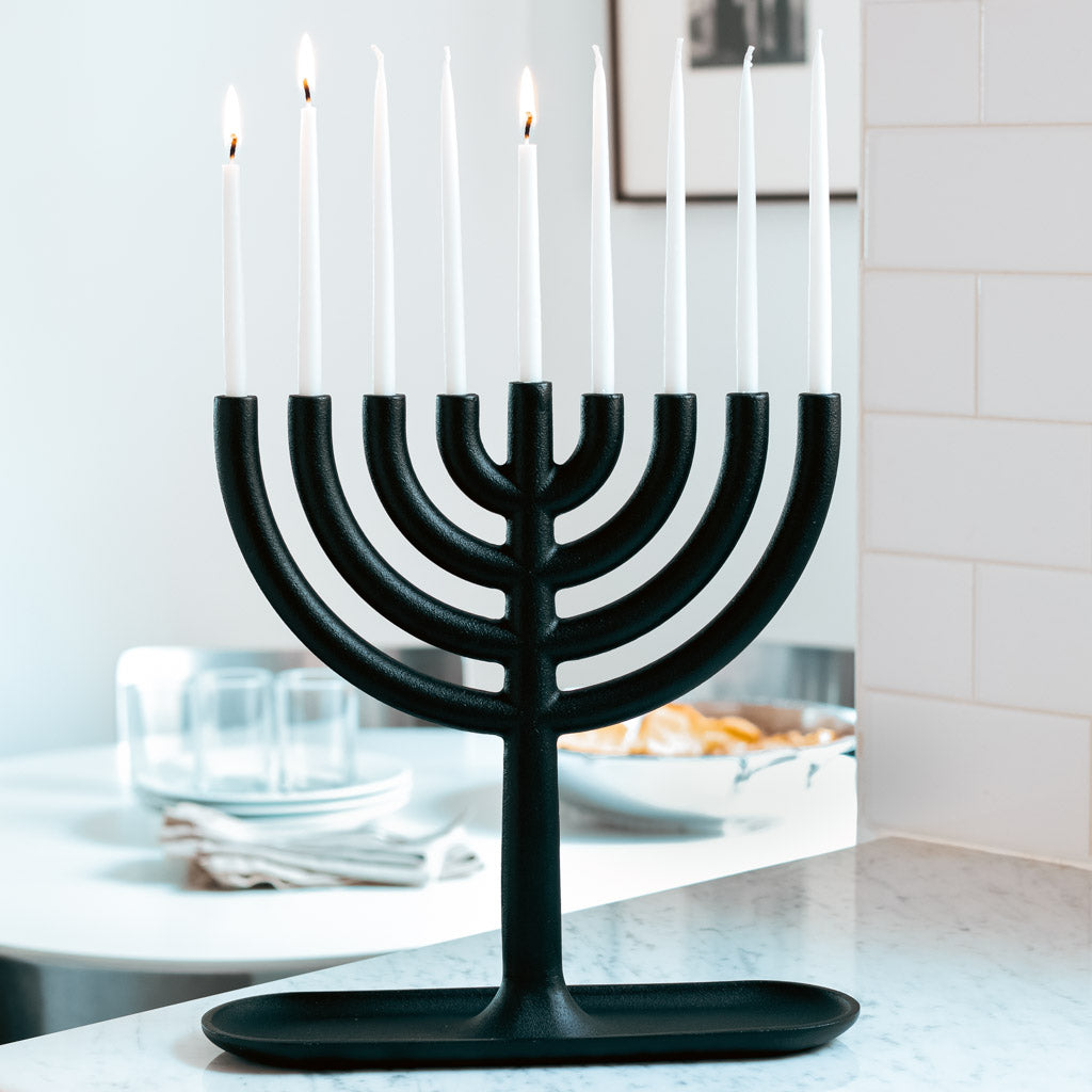 Black cast iron Hanukkah menorah by Josh Owen with white taper candles, 11"L x 11"H.