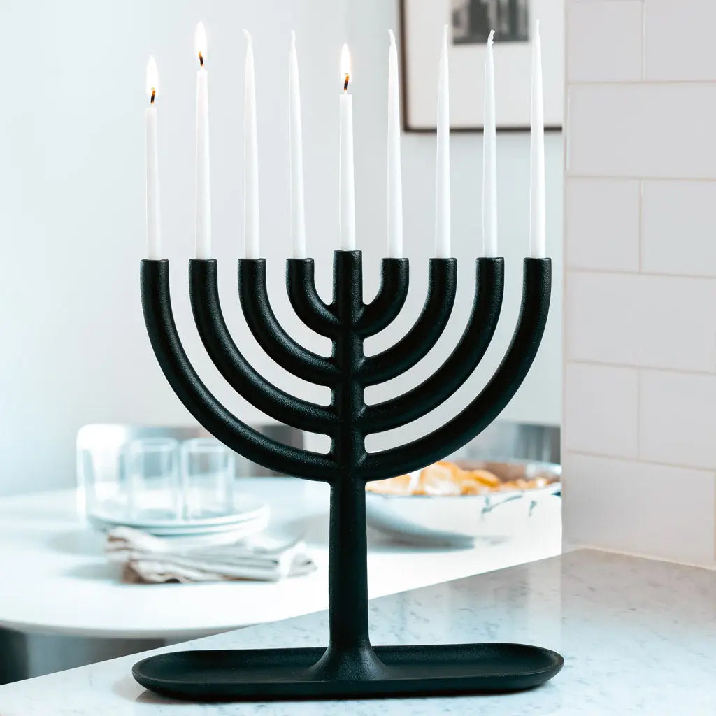 Black cast iron Hanukkah menorah by Josh Owen with white taper candles, 11"L x 11"H.
