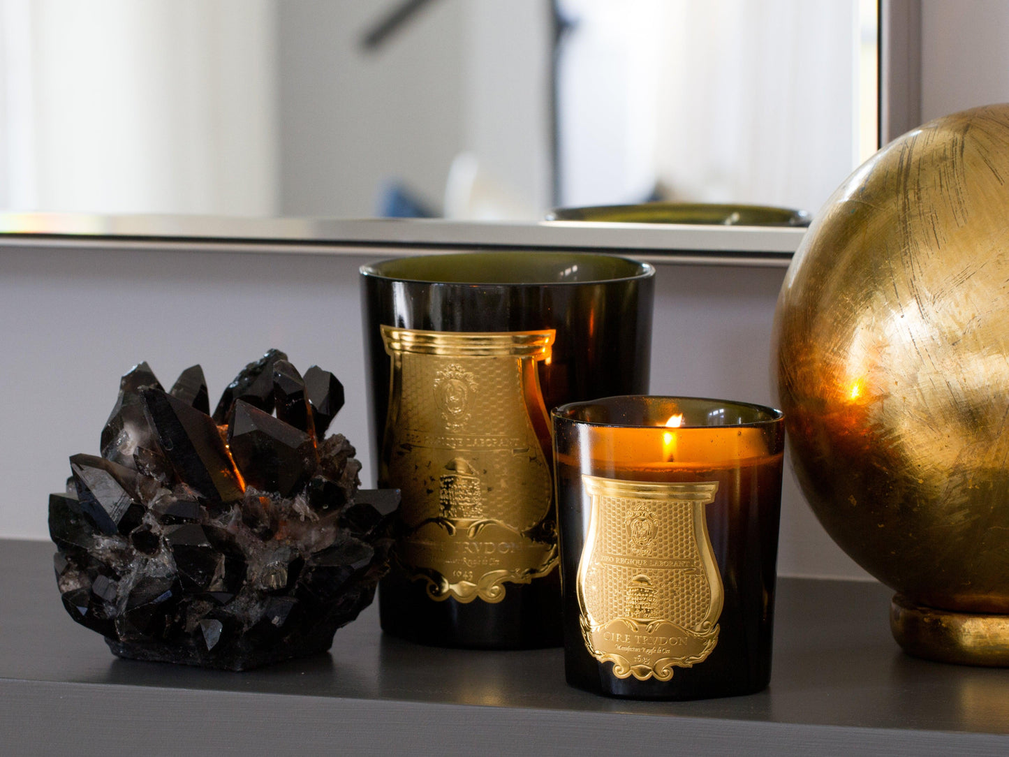 Black classic quartz votive candle holder with raw crystals, next to two dark glass candles and a golden sphere.