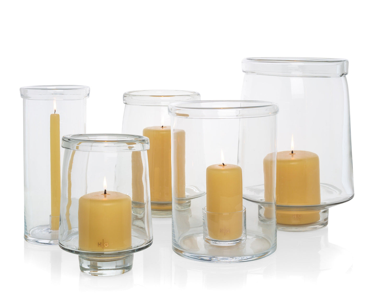 Clear glass Antwerp hurricane candle holders in three sizes, some with lit yellow pillar candles.