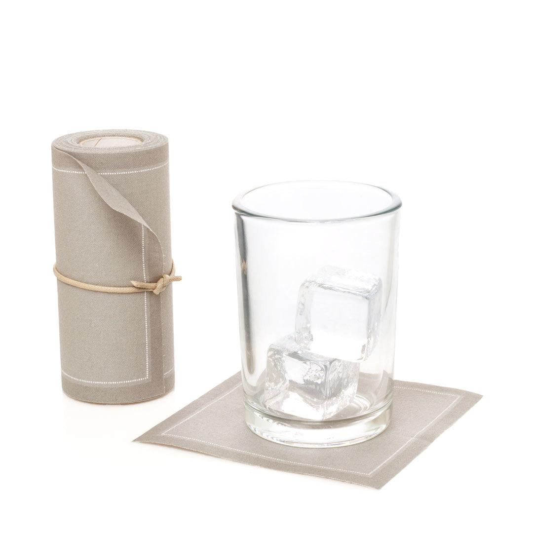 Sand tear-off cotton cocktail napkin roll with one napkin under a glass of ice.