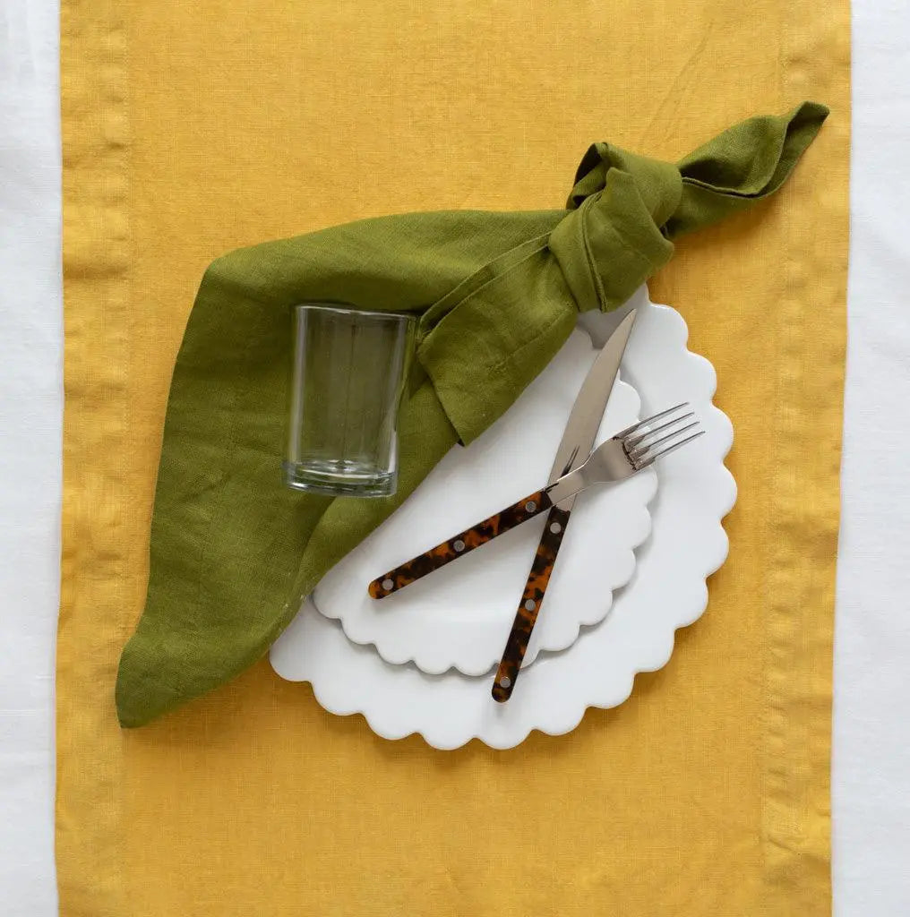 White ceramic scalloped dinner plate with salad plate, green linen napkin, clear glass, and tortoise-handle flatware.