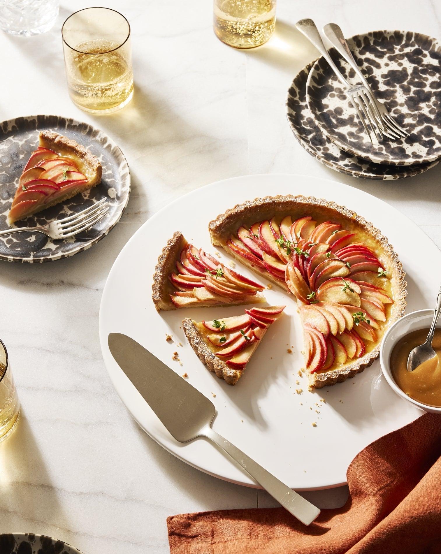 Sliced apple tart with caramel sauce, drinks, and leopard print plates for Thanksgiving desserts.