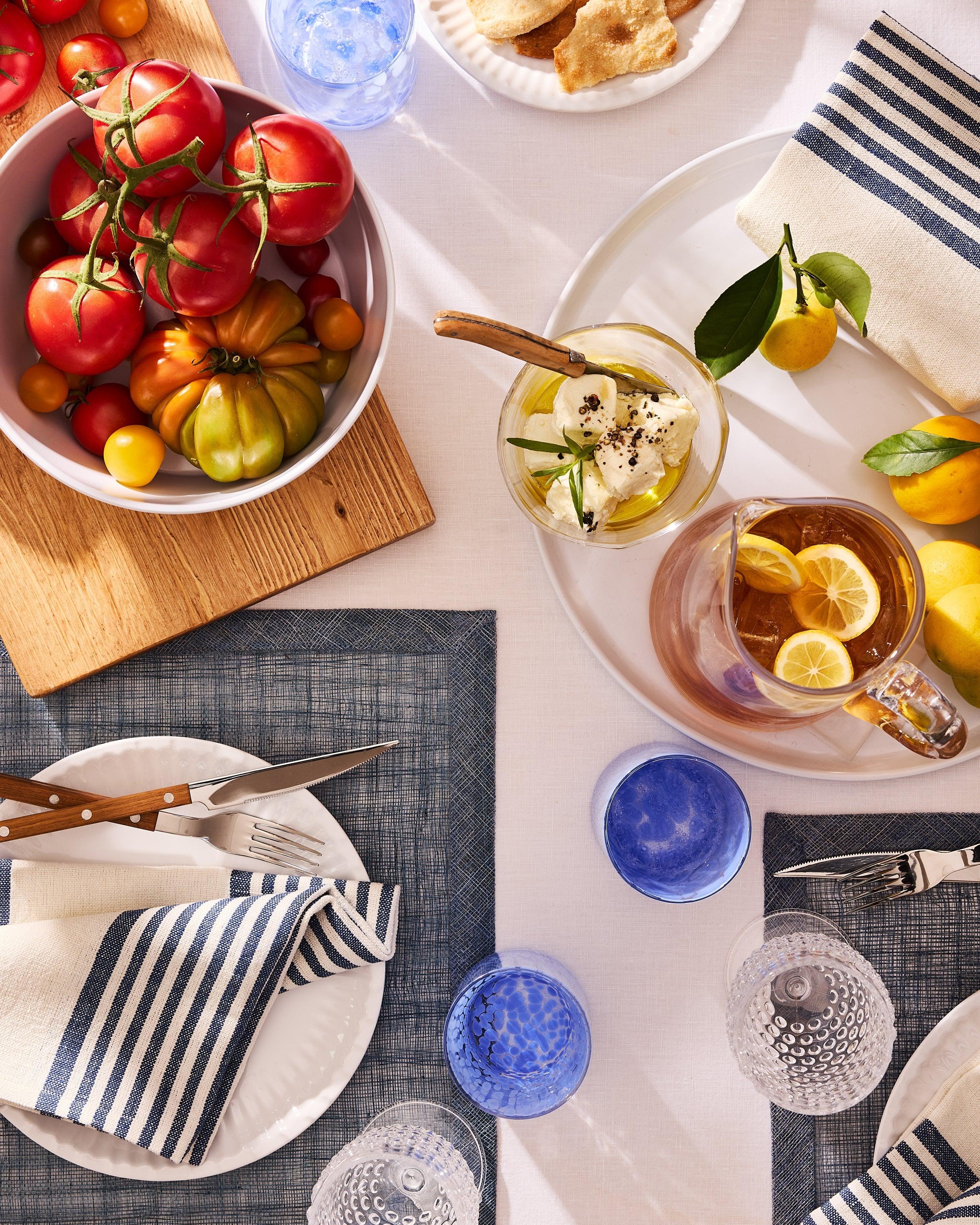 Summer table setting by Hudson Grace with fresh tomatoes, iced tea, blue striped linens, and glassware.