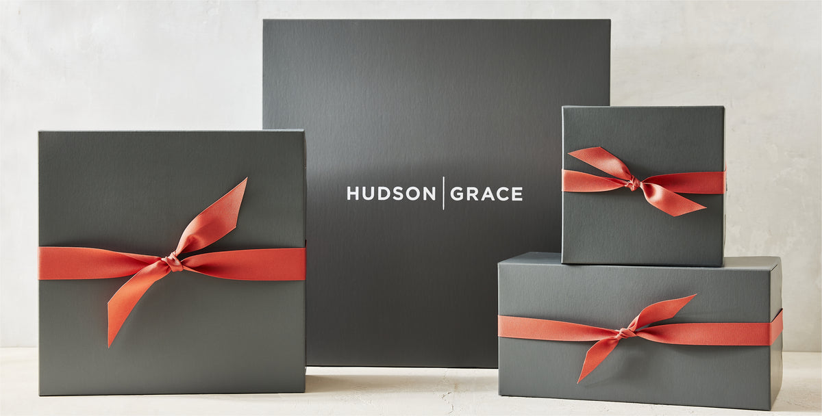 Three charcoal grey Hudson Grace gift boxes tied with elegant red satin ribbons.