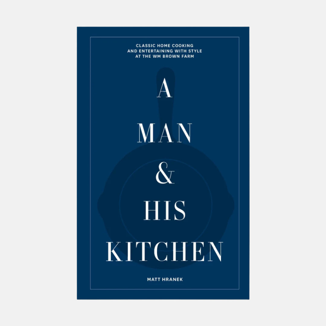 A Man & His Kitchen" hardcover cookbook with dark blue cover, white text, and subtle cast iron pan graphic.