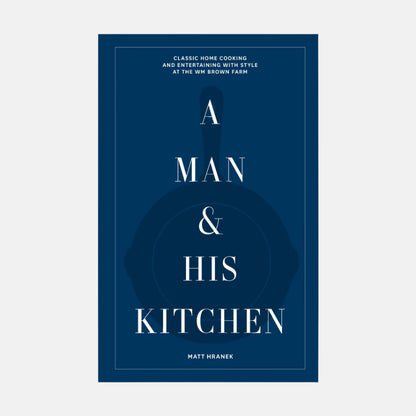 A Man & His Kitchen" hardcover cookbook with dark blue cover, white text, and subtle cast iron pan graphic.