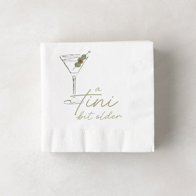 White 3-ply paper cocktail napkins with a martini glass and "a tini bit older" in olive green.