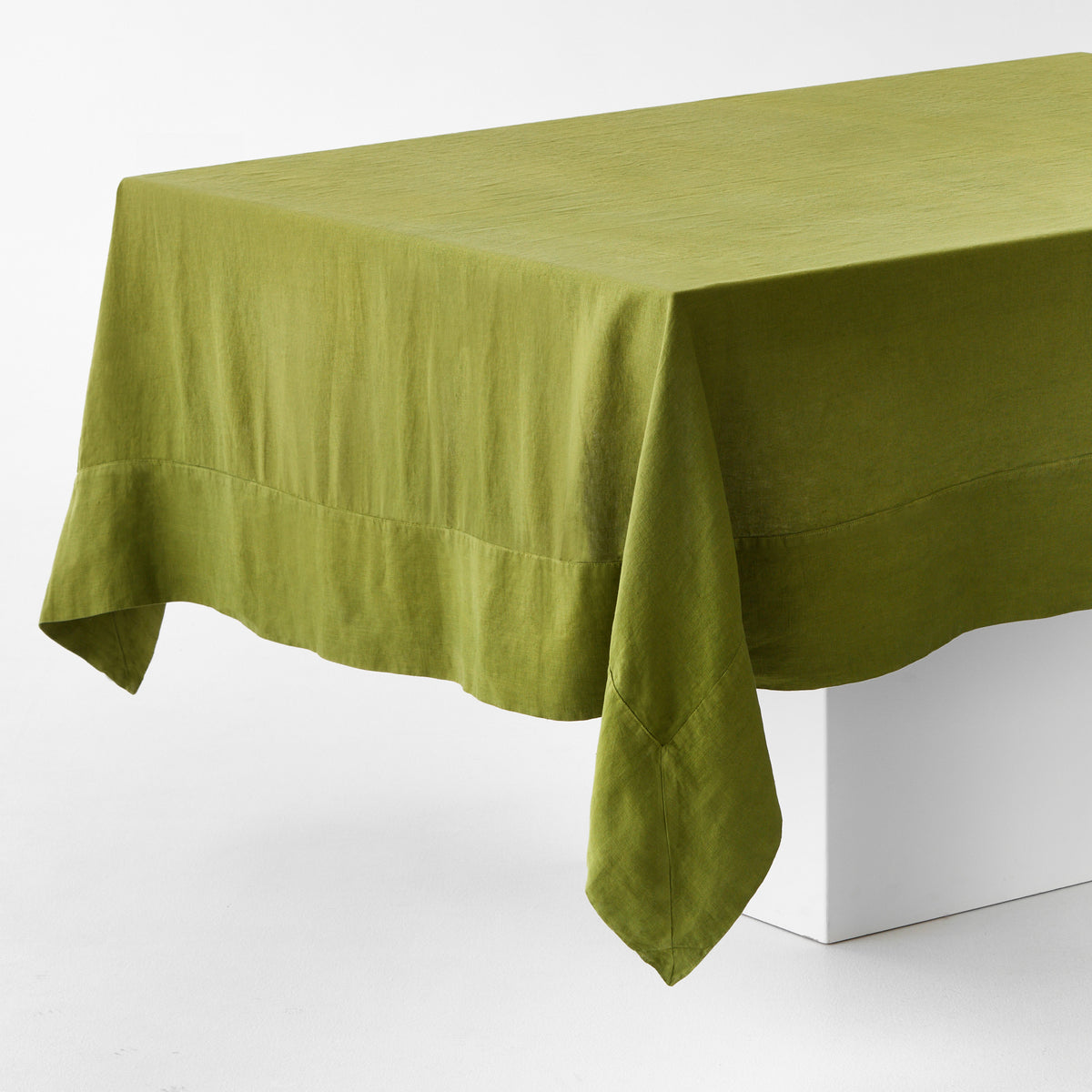 Aloe green hand-dyed 100% linen tablecloth with mitered corner detailing draped over a white table.