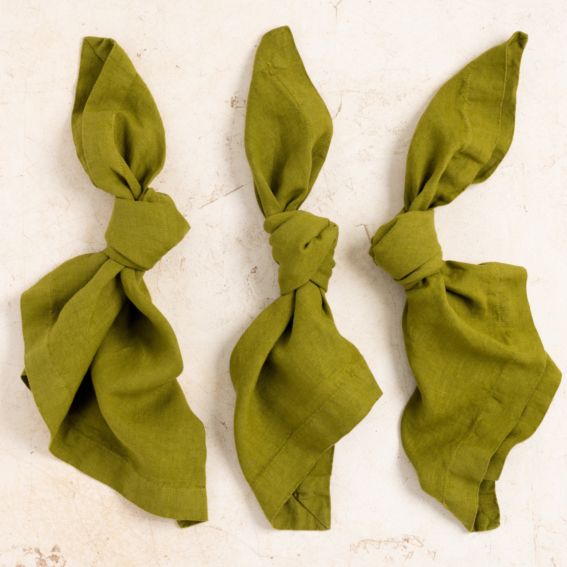 Three Aloe green HG Signature hand-dyed 22-inch linen napkins, knotted, on a light background.