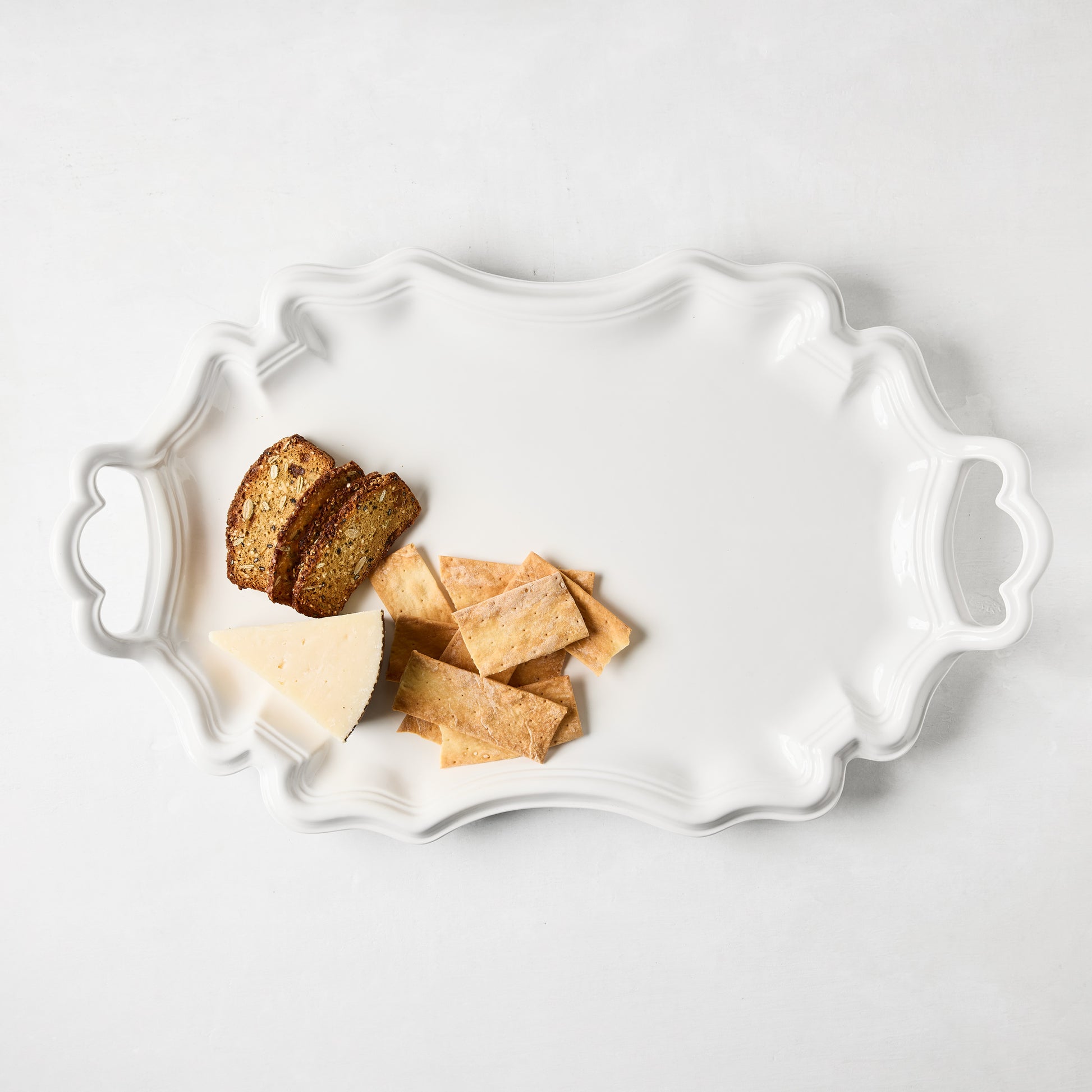 White ceramic Amalfi serving platter with scalloped edges and integrated handles, holding cheese and crackers.