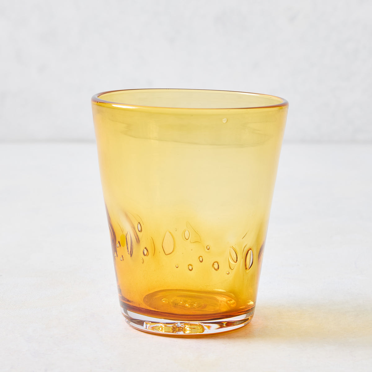 Amber Henri mouth-blown 8 oz drinking glass in translucent yellow with unique glass-blown air bubbles and organic shape.