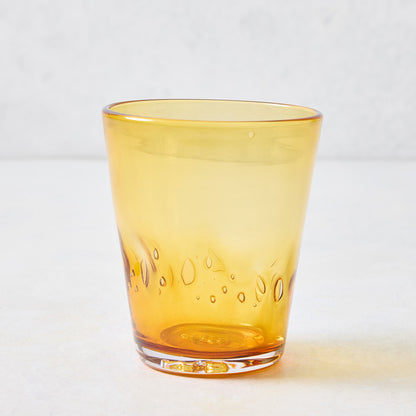 Amber Henri mouth-blown 8 oz drinking glass in translucent yellow with unique glass-blown air bubbles and organic shape.