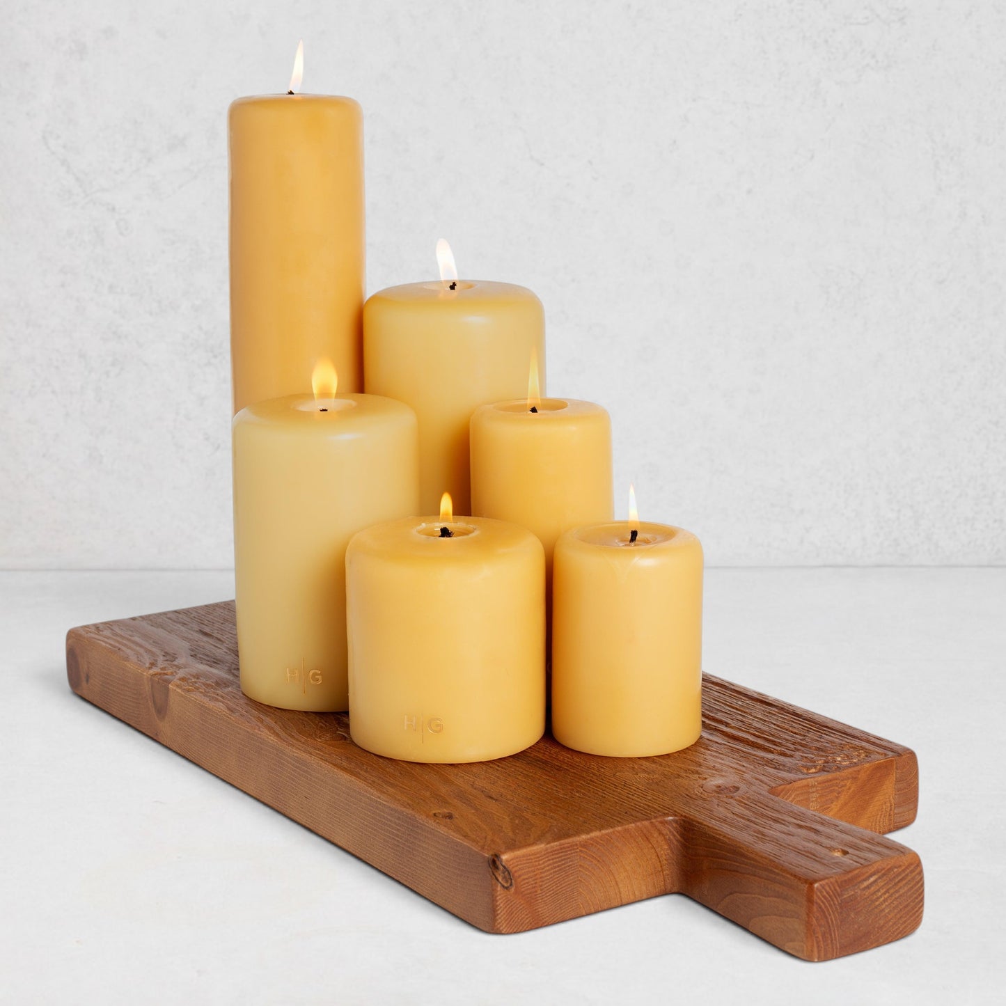 Five lit HG Amber paraffin pillar candles on a wooden board.