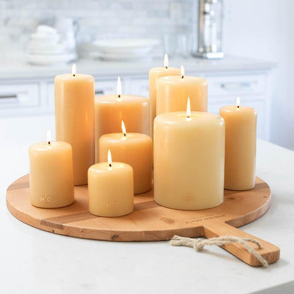 HG Amber Unscented Pillar Candle, 3"x4", with gold HG logo, on a wooden board with other amber candles.
