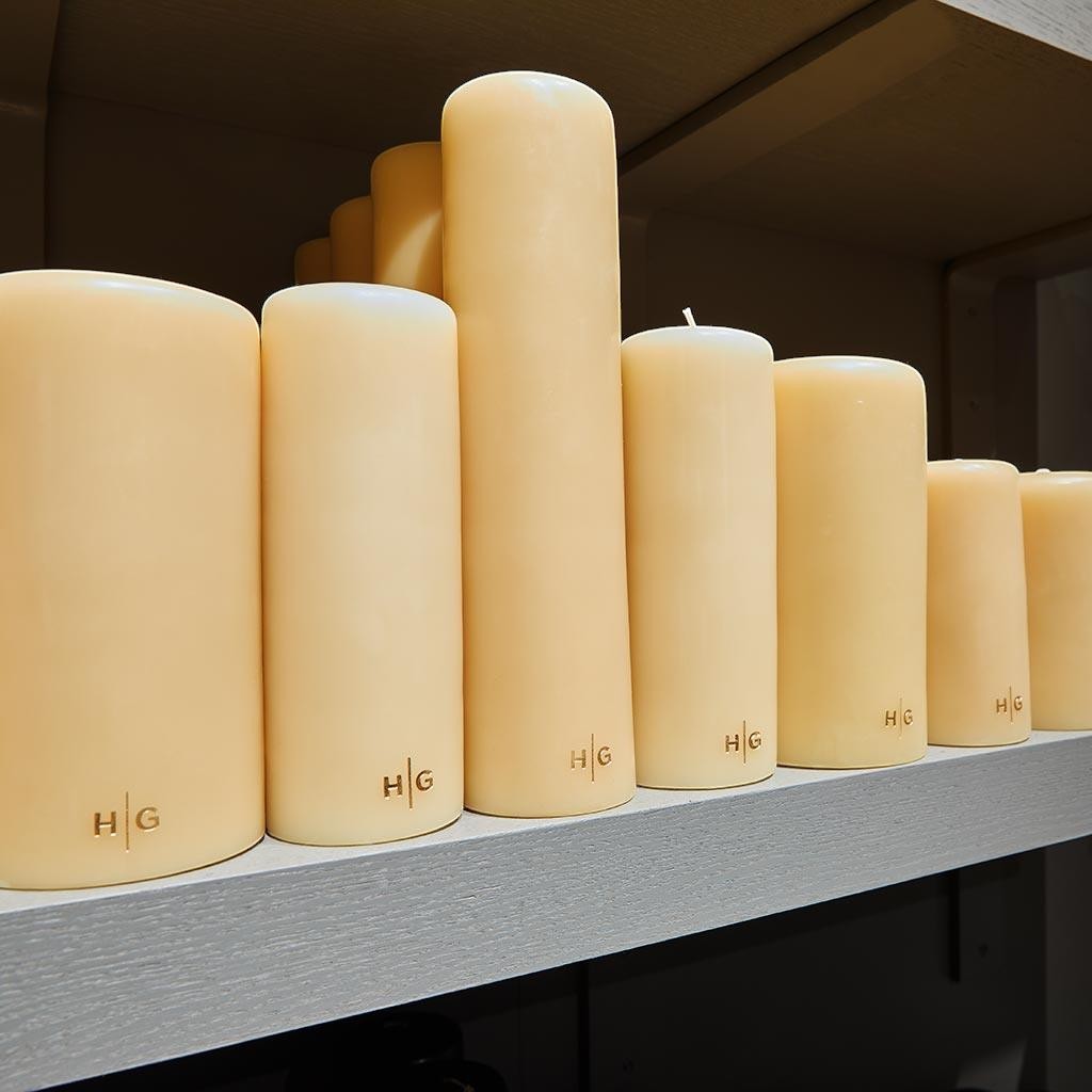 HG Amber Unscented Pillar Candles, 3"x4" paraffin, with gold HG logo, on a shelf.