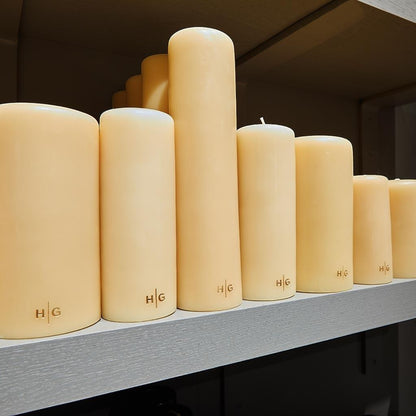 HG Amber Unscented Pillar Candles, 3"x4" paraffin, with gold HG logo, on a shelf.