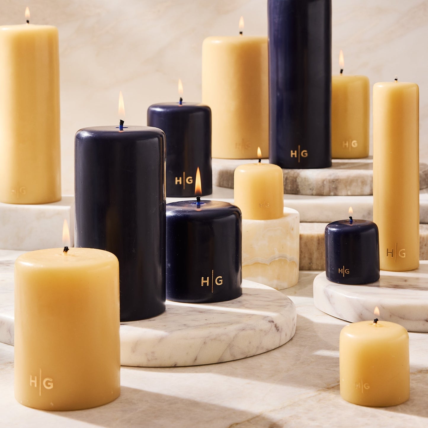 HG Amber Unscented Pillar Candle, 3"x8", with a gold HG logo, alongside other amber and black candles.