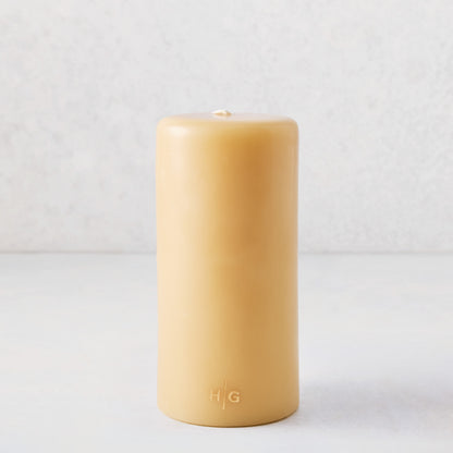 Amber unscented pillar candle, 3x8 inches, made of natural resin-tinted paraffin with a gold HG logo embossed at the base.