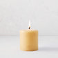 4x4 inch amber pillar candle with a lit cotton wick and embossed gold HG logo on a light background.