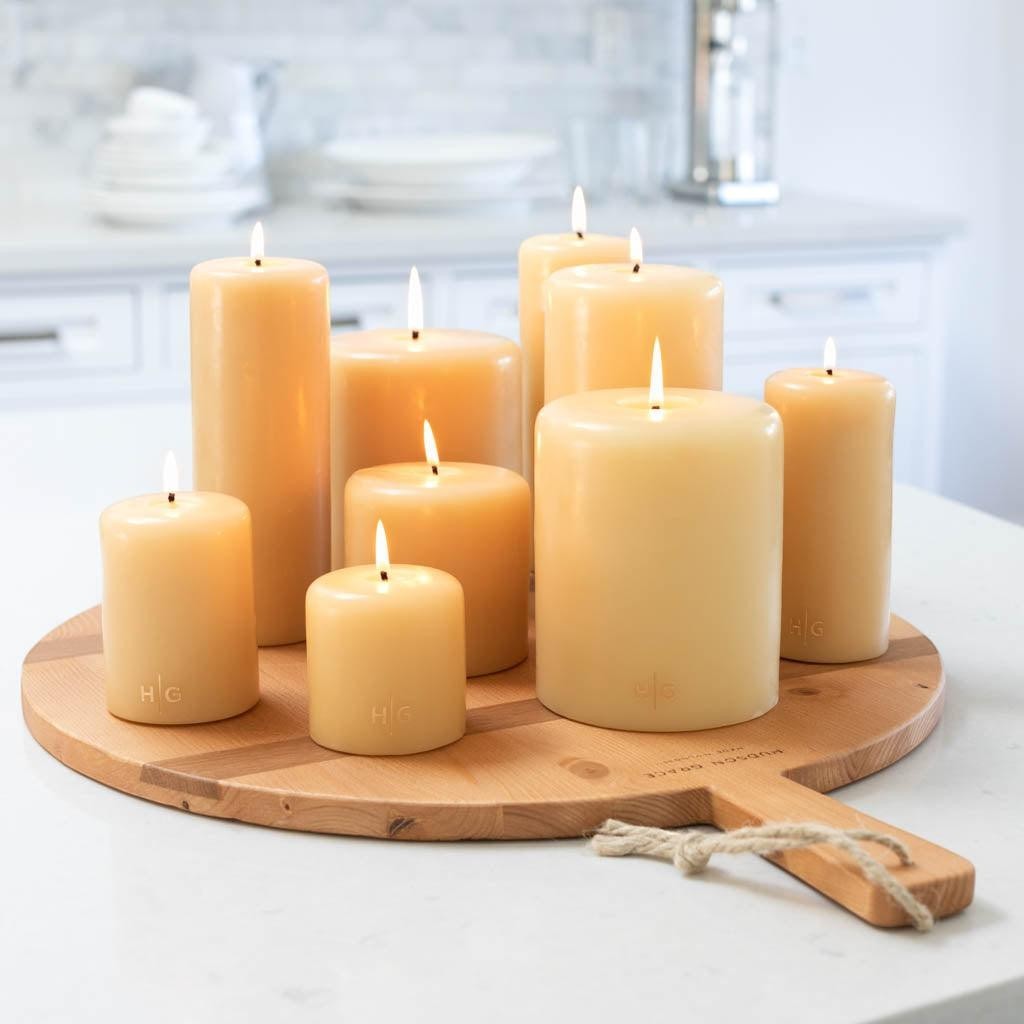 HG Amber unscented paraffin pillar candles, various sizes, with gold HG logo, on a wood board.