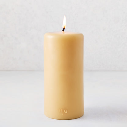 4x8 inch amber unscented pillar candle with a lit cotton wick and gold embossed HG logo on a light background.